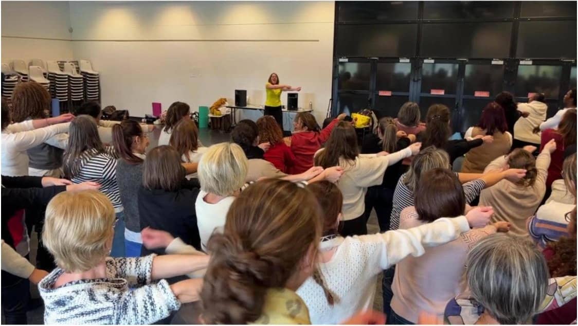 Nathalie Chiffoleau anime une séance de yoga du rire devant un grand groupe, bras tendus